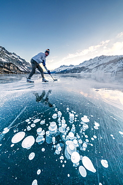 Man playing ice hockey on frozen Lake Sils, Engadine, canton of Graubunden, Switzerland, Europe