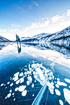 Man playing ice hockey on frozen Lake Sils covered of bubbles, Engadine, canton of Graubunden, Switzerland, Europe