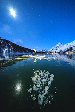 Full moon on ice skater on frozen Lake Sils lit by head torch, Engadine, canton of Graubunden, Switzerland, Europe