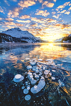 Clouds in the burning sky at sunset on Piz Da La Margna and ice bubbles trapped in Lake Sils, Engadine, Graubunden, Switzerland, Europe