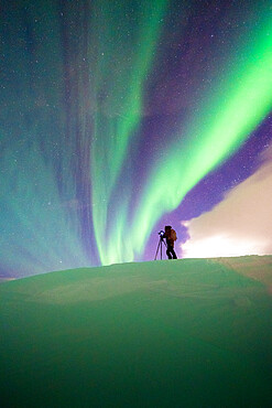 Man with tripod photographing the Northern Lights (Aurora Borealis) standing in the snow, Skarsvag, Nordkapp, Troms og Finnmark, Norway, Scandinavia, Europe