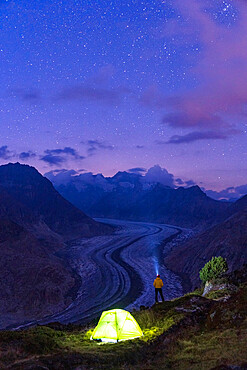 Hiker man with head torch lighting up the starry sky near tent by the Aletsch Glacier, Bernese Alps, Valais canton, Switzerland, Europe