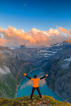 Man with outstretched arms enjoying sunset over lake Limmernsee standing on top of rocks, Canton of Glarus, Switzerland, Europe