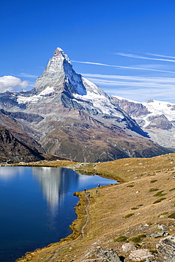 Hikers walking on the path beside the Stellisee with the Matterhorn reflected, Zermatt, Canton of Valais, Pennine Alps, Swiss Alps, Switzerland, Europe