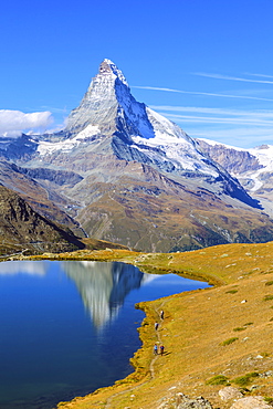 Hikers walking on the path beside the Stellisee with the Matterhorn reflected, Zermatt, Canton of Valais, Pennine Alps, Swiss Alps, Switzerland, Europe