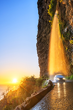 Car passing under Anjos waterfall on slippery coastal road at sunset, Ponta do Sol, Madeira island, Portugal, Atlantic, Europe