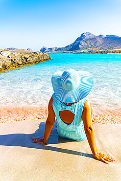 Back view of woman contemplating the sea sitting on pink sand of Falassarna beach, Kissamos, Chania, Crete, Greek Islands, Greece, Europe