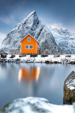 Rorbu in the snow at foot of Olstind mountain overlooking the Arctic Sea, Sakrisoy, Reine, Nordland, Lofoten Islands, Norway, Scandinavia, Europe