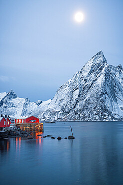 Red Rorbu cabins and majestic Olstind peak lit by moon during winter dusk, Hamnoy, Nordland county, Lofoten Islands, Norway, Scandinavia, Europe