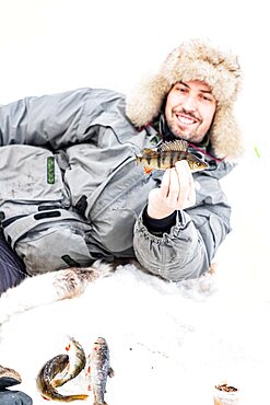 Portrait of smiling man holding a fish caught after ice fishing, Lapland, Sweden