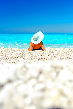 Woman with straw hat contemplating the sea lying on a beach in summer, Kefalonia, Ionian Islands, Greek Islands, Greece, Europe