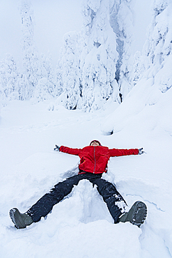 Cheerful woman smiling lying down in the snow, Lapland, Finland, Europe