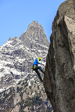 Climber on steep rock face in the background blue sky and peaks of the Alps, Masino Valley, Valtellina, Lombardy, Italy, Europe