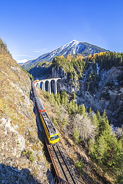 Bernina Express passes over the Landwasser Viadukt surrounded by colorful woods, Canton of Graubunden, Switzerland, Europe