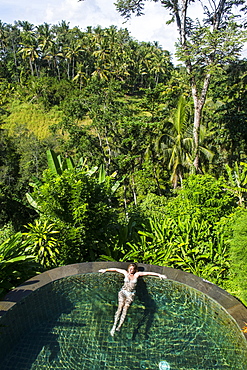 Woman enjoying an overflowing pool above a valley in the Kamandalu Ubud resort, Ubud, Bali, Indonesia, Southeast Asia, Asia