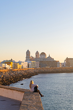 Woman enjoying the view of Santa Cruz Cathedral and ocean seen from the promenade along quayside, Cadiz, Andalusia, Spain, Europe