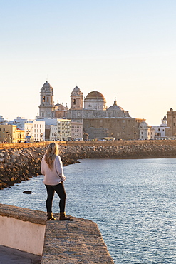 Woman enjoying the view of Santa Cruz Cathedral and ocean seen from the promenade along quayside, Cadiz, Andalusia, Spain, Europe