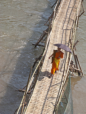 LAOSMONK ON A BRIDGE CROSSING A RIVER IN THE HOLY CITY OF LUANG PRABANG