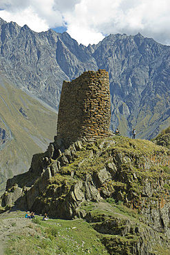 Tourists trekking by a tower near the Gergeti Holy Trinity Church by the river Chkheri, under Mount Kazbegi at an elevation of 2170 meters in the Caucasus, Georgia, Central Asia, Asia