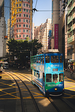 A vertical image of a Tram going through the sun on Johnstone Road in Hong Kong