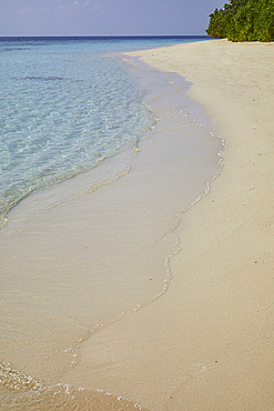Pristine shallow waters lap against the white coral sand of a tropical beach; Havodda Island, in the far south of the Maldives, Gaafu Dhaalu atoll, Indian Ocean.