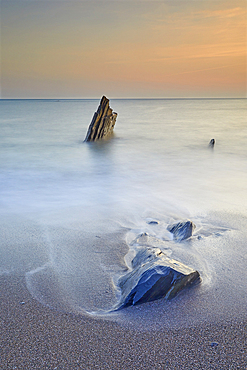 Surf rolls around shoreline rocks at sunset, in Ayrmer Cove, a remote cove near Kingsbridge, south coast of Devon, England, United Kingdom, Europe