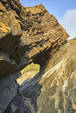 A sunlit view of a rock arch, formed from multiple layers of red sedimentary rock, at Hartland Quay, on the Atlantic coast of Devon, England, United Kingdom, Europe