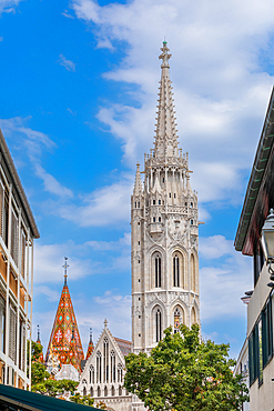 Street-level view of the Gothic Matthias Church tower and spire framed by nearby buildings in the Castle District. Vertical portrait orientation.