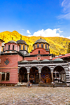 Golden hour light casting a warm glow over the domes and striped arches of the Rila Monastery in Bulgaria.