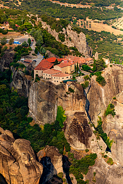 Aerial view in vertical orientation of a Meteora monastery perched on a high rock formation, surrounded by dramatic cliffs and greenery, Thessaly, Greece.