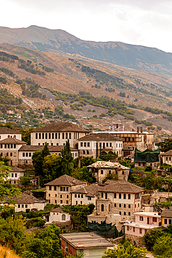 Vertical orientation view of traditional stone-roofed buildings in Gjirokastër with the mountains of southern Albania in the background.