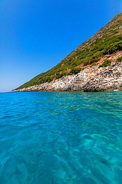 Clear turquoise waters of the Ionian Sea meeting rocky, vegetation-covered coastline near Dhermi, Vlorë County, Albania, on a bright summer day.