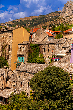 Close-up view of stone buildings with slate roofs in the Old Town of Mostar, nestled against the hillside with colorful accents and historic charm.
