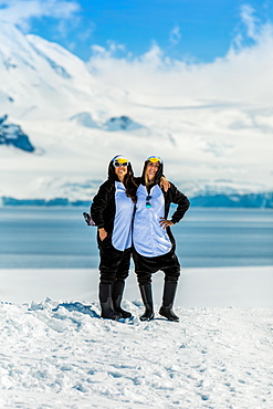 Two American women tourists in Penguin Onesies on sunny day, posing on the glaciers, Antarctica, Polar Regions