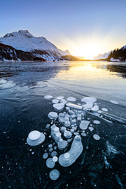 Methane bubbles in the icy surface of Silsersee with snowy peak illuminated by sunset light, Lake Sils, Engadine Valley, canton of Graubunden, Switzerland, Europe