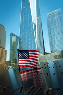 A small American flag at the 9/11 Memorial Park in New York City with the new World Trade Centre rising in the background, New York, United States of America, North America