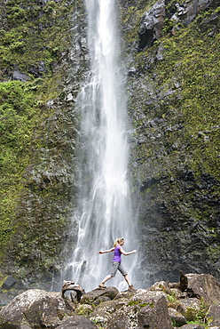 Hiker leaping in front of a waterfall along the famous Kalalau Trail, along Kauai's Na Pali Coast, Kauai, Hawaii, United States of America, North America