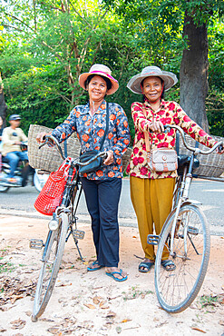 Two local women with their bicycles smiling together in Siem Reap, Cambodia, Indochina, Southeast Asia, Asia