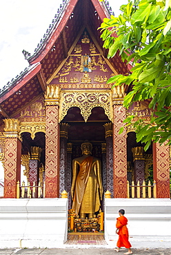 A young Buddhist monk stands before a large statue of Golden Buddha in Luang Prabang, Laos, Indochina, Southeast Asia, Asia