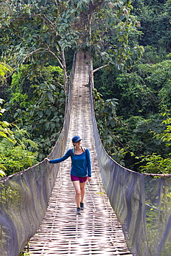 A woman crosses a precarious looking suspension bridge over the jungle in Laos, Indochina, Southeast Asia, Asia