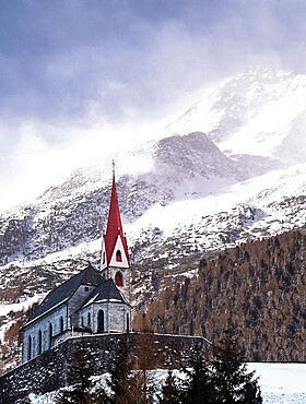 Church with a snowy mountains in the background with wind gusting on slopes and top, Trentino-Alto Adige, Italy, Europe