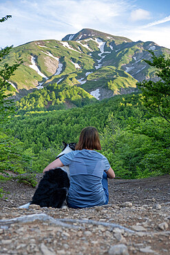 A girl sitting beside and hugging her border collie dog staring at a mountain landscape of Cusna Mountain, Emilia Romagna, Italy, Europe