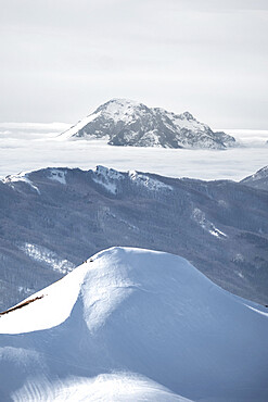 Snowy mountain emerging from fog in the background and snow covered hill in the foreground, Emilia Romagna, Italy, Europe