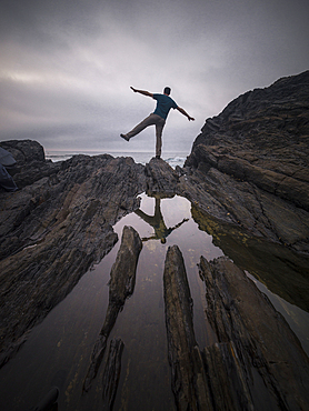 A man balancing on one leg on the rocks and his reflection in a pond of water, Spain, Europe