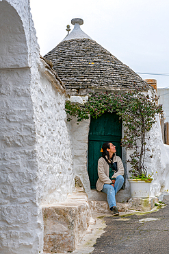 Woman tourist sit on the front of one Trullo traditional house with conic shape ceiling, UNESCO World Heritage Site, Alberobello, Apulia, Italy, Europe