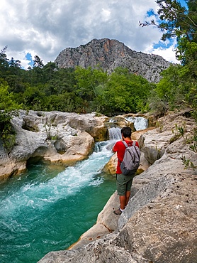 Man photographing Yazili canyon waterfall with mountains in the background on a cloudy day, in Turkey