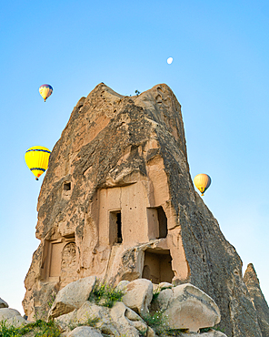 Beautiful cave inside a rock formation in Cappadocia at sunrise with hot air balloons in the air, in Turkey