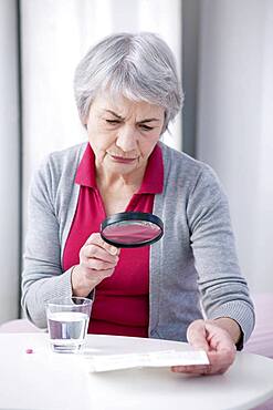 Senior woman reading medication instruction sheet with a magnifying glass.