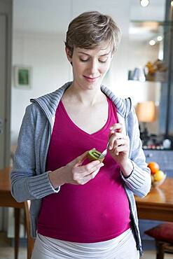 Pregnant woman eating a kiwi.