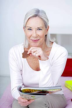 Senior woman nibbling while reading a magazine.